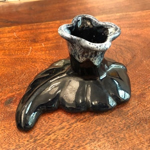 Może przedstawiać: Czarny ceramiczny świecznik w kształcie liścia z górną częścią w kształcie kwiatu. Świecznik ma błyszczące wykończenie i białe akcenty.