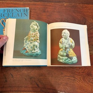 May include: Open book with images of antique porcelain figurines. The figurines are seated, with detailed clothing and facial features. The book's cover reads "FRENCH PORCELAIN" in blue and white.