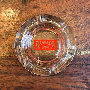 May include: A clear glass ashtray with a red "Ramada Inn" logo.