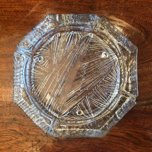 Puede incluir: Cenicero octogonal de vidrio con un diseño texturizado y grabado. El cenicero es transparente y tiene un aspecto ligeramente esmerilado.