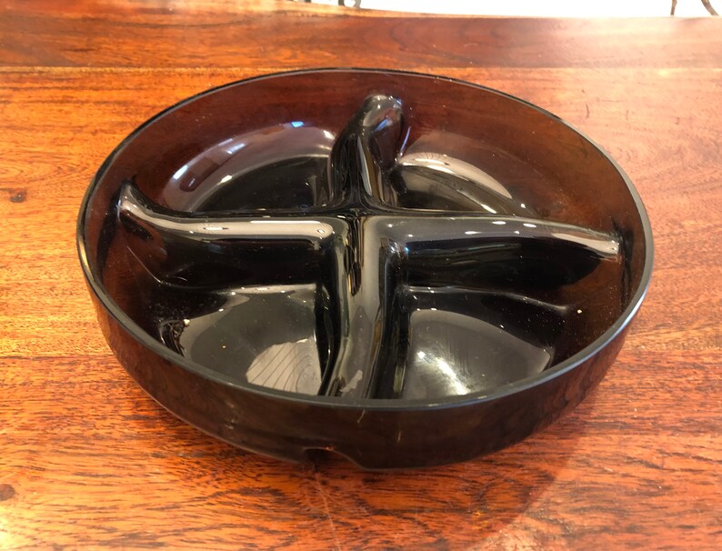 May include: A dark brown glass divided dish with four sections. The dish is round and has a smooth, glossy finish.