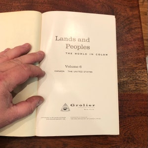 May include: A white book with the title "Lands and Peoples" and the subtitle "The World in Colour". The book is volume 6 and covers Canada and the United States. The Grolier Incorporated logo is at the bottom of the page.