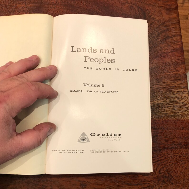 May include: A white book with the title "Lands and Peoples" and the subtitle "The World in Colour". The book is volume 6 and covers Canada and the United States. The Grolier Incorporated logo is at the bottom of the page.
