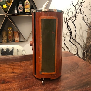 May include: A vintage, cylindrical, metal, orange and green, wall-mounted, decorative object with a silver top.