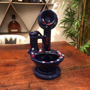 Könnte beinhalten: Ein blauer und weißer Keramik-Toiletten-Blumentopf mit roten Punkten. Die Toilette hat ein Telefonhörer oben und einen Wasserhahn an der Seite.