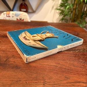 May include: A vintage book titled "French Porcelain Treasures and Treasures" with a blue cover and an illustration of a porcelain object. The book is by Landais and published by Putnam.