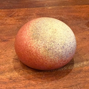 Peut inclure: Objet sphérique et tacheté, avec un dégradé de couleurs allant du rouge-orangé au blanc pâle. La surface est texturée. L'objet repose sur une surface en bois. L'objet est de forme ronde.