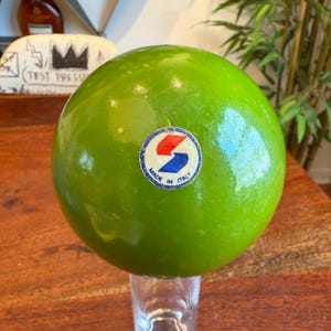 Op de afbeelding: Een groene rubberen bal met een witte sticker waarop "Made in Italy" staat en een blauwe en rode letter "S".