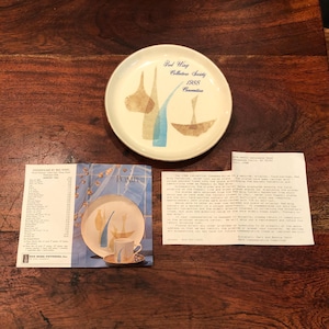 Puede incluir: Un plato conmemorativo de la Convención de la Red Wing Collectors Society de 1988 con un diseño azul y amarillo. El plato está sobre una superficie de madera con un folleto sobre la convención.