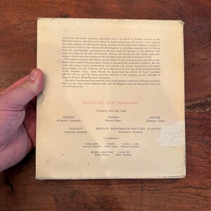May include: A vintage book cover with the title "Pleasures and Treasures" in red text. The cover lists various topics like shells, clocks, silver, tartans, and firearms. The book appears to be about antique collecting.