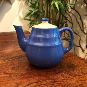 May include: A small blue teapot with a white lid. The teapot has a rounded body and a curved spout. It is sitting on a wooden surface.