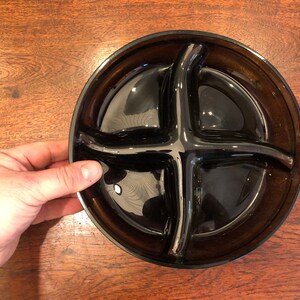 May include: A black glass serving dish with four divided sections. The dish is round and has a slightly raised rim.