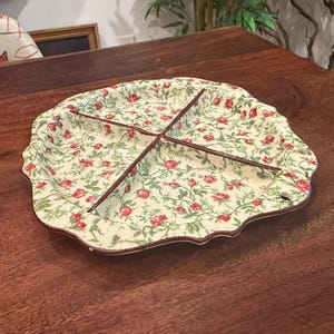 Może przedstawiać: Kwiatowy talerz do serwowania z czterema podzielonymi sekcjami. Kremowa powierzchnia pokryta jest wzorem czerwonych róż i zielonych liści. Obręcz i przegrody są w kolorze ciemnobrązowym. Talerz ma falisty brzeg.