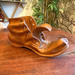 May include: A handcrafted wooden boot sculpture, showcasing intricate details and a warm, natural wood tone. The boot features a classic design with visible stitching and rivet details, perfect for home decor.