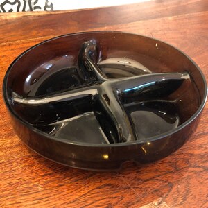May include: A dark brown glass divided serving dish with four sections. The dish is round and has a slightly raised rim.