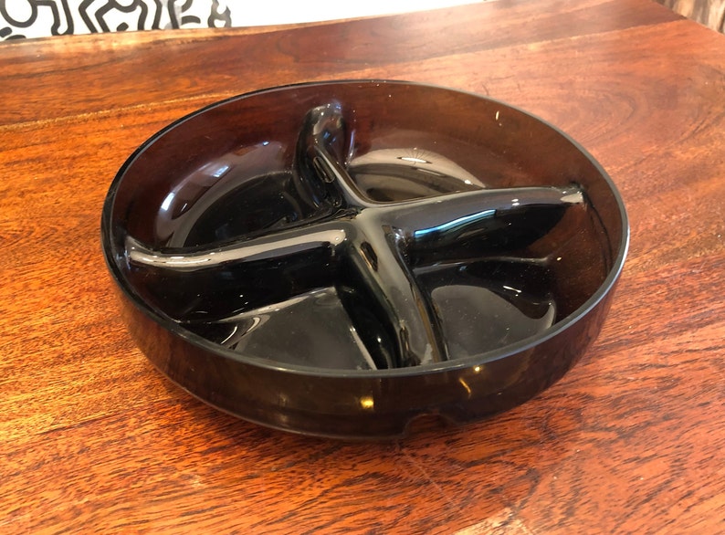 May include: A dark brown glass divided serving dish with four sections. The dish is round and has a slightly raised rim.