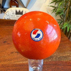 Puede incluir: Esfera naranja con un logotipo azul y rojo que dice "Made in Italy".
