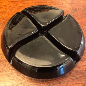 May include: A black glass divided dish with four sections. The dish is round and has a glossy finish.