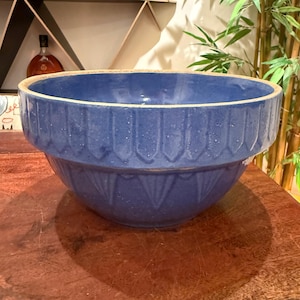 Peut inclure: Un grand bol mélangeur en céramique bleue, doté d'un bord beige épais non émaillé et d'un extérieur texturé avec des indentations verticales en forme de pétales pointus sur la moitié supérieure et un motif triangulaire répété.