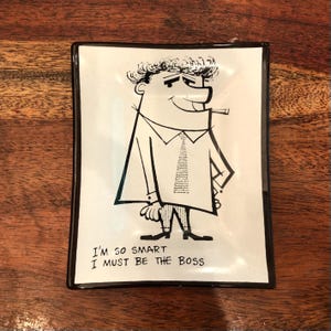 May include: Black and white illustration of a man with a mustache and a tie, smoking a pipe. The illustration is on a white rectangular tray with a black border. The text "I'm so smart I must be the boss" is printed below the illustration.