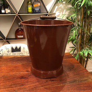 May include: A brown metal bucket with a wooden handle. The bucket is sitting on a wooden surface.