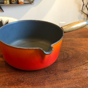 May include: Orange and gray enameled cast iron saucepan with a wooden handle.