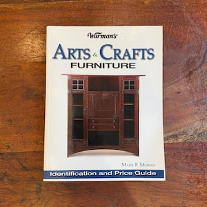 May include: A book titled "Warman's Arts & Crafts Furniture" with a picture of a wooden cabinet on the cover. The book is a price guide and identification resource by Mark F. Moran. The cover is white with blue and red text.