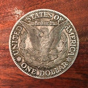 Op de afbeelding: Een zilveren Amerikaanse dollarmunt met een adelaar en de woorden "United States of America" en "In God We Trust".