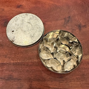 May include: A round metal tin container with a separate lid, containing a collection of various small, silver-toned metal cookie cutters in different animal and shape silhouettes, arranged compactly within the circular base of the container.