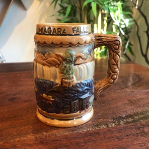 May include: A brown ceramic beer stein with a scene of Niagara Falls and the text "NIAGARA FALLS" on the front. The stein has a handle with a carved design.