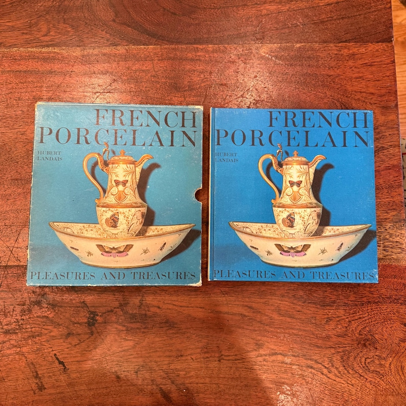 May include: Two vintage books titled "French Porcelain" by Hubert Landais. Each book cover features a blue background with a gold teapot and a matching basin. The words "Pleasures and Treasures" are printed at the bottom of each book.