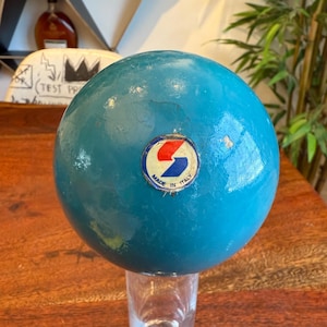 Può includere: Una sfera blu turchese con un adesivo bianco e rosso che dice "Made in Italy" e un logo blu e rosso con una S stilizzata.