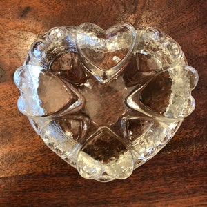 Puede incluir: Un plato de vidrio transparente en forma de corazón con una superficie texturizada. El plato está formado por formas de corazón más pequeñas.