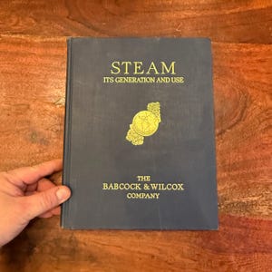 May include: A blue hardback book titled "STEAM ITS GENERATION AND USE" with gold lettering. The book is published by The Babcock & Wilcox Company and features a gold globe illustration on the cover.
