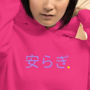 May include: A magenta hoodie with a drawstring hood and a kangaroo pocket. The front of the hoodie features Japanese characters in a light blue color. The background includes a plane interior with porthole windows.