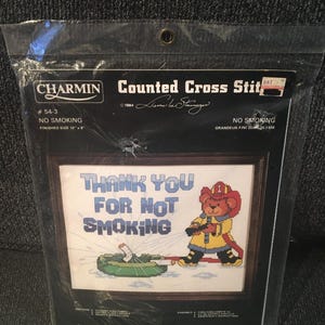 May include: A Charmin counted cross stitch kit, featuring a framed design with the text "THANK YOU FOR NOT SMOKING." The image includes a cartoon firefighter bear extinguishing a cigarette. Finished size is 10" x 8".