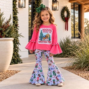 May include: A bright pink long-sleeve shirt with ruffled bell sleeves and a graphic print that reads Rocking Around The Christmas Tree, paired with white bell-bottom pants featuring a repeating pattern of cowboy boots, hats, and stars.