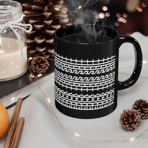 Könnte beinhalten: Schwarze Keramik-Kaffeetasse mit einem weißen geometrischen Muster aus Wellen und Linien. Die Tasse ist mit Kaffee gefüllt und Dampf steigt aus der Oberseite auf.