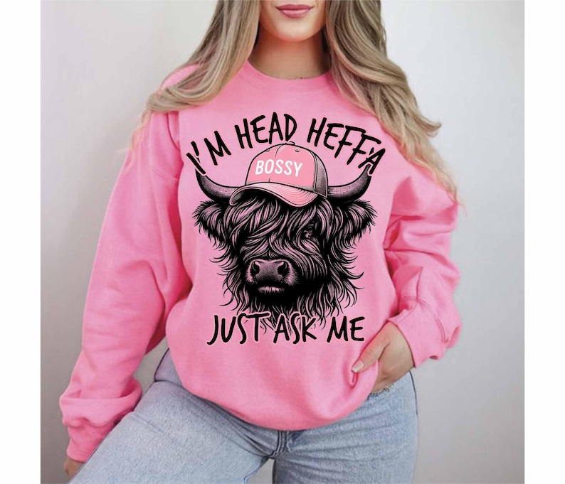 May include: Pink sweatshirt with a black and white illustration of a Highland cow wearing a pink hat that says "Bossy". The text on the sweatshirt reads "I'm Head Heffa Just Ask Me".