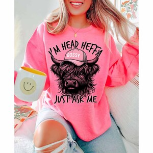 May include: A pink sweatshirt with a black highland cow wearing a hat that says "Bossy" and the text "I'm Head Heffa Just Ask Me".