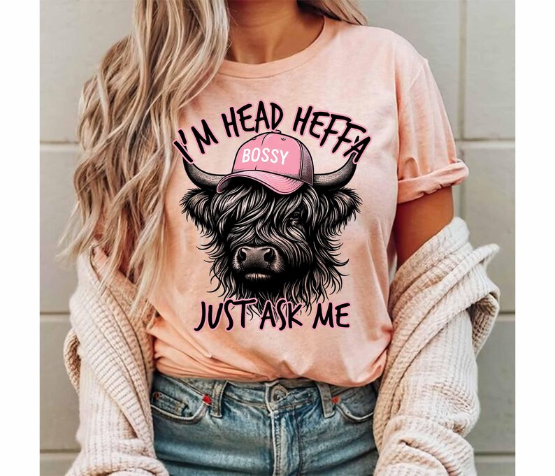 May include: A pink t-shirt with a black and white illustration of a Highland cow wearing a pink hat that says "Bossy". The text on the shirt reads "I'm Head Heffa Just Ask Me".