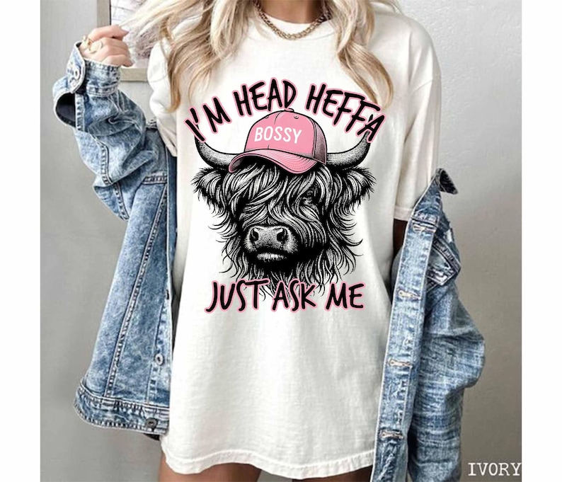 May include: White t-shirt with a black and white illustration of a Highland cow wearing a pink hat that says "Bossy". The text "I'm Head Heffa Just Ask Me" is printed below the cow.