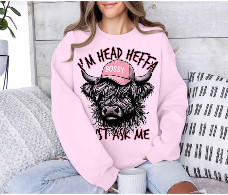 May include: Pink sweatshirt with a black and white Highland cow wearing a pink hat that says "Bossy" and the text "I'm Head Heffa Don't Ask Me".