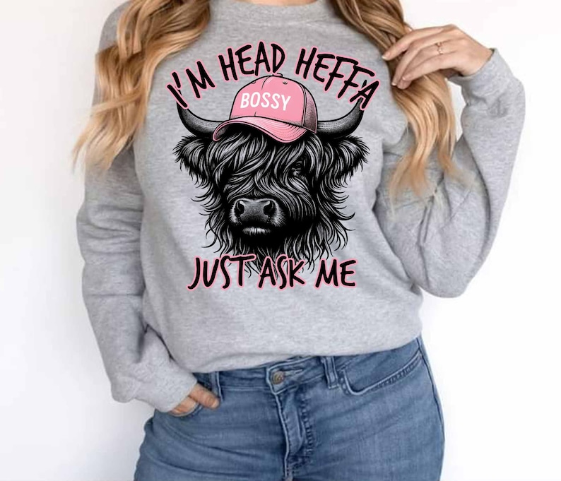 May include: Gray sweatshirt with a black and white illustration of a Highland cow wearing a pink hat that says "Bossy". The text "I'm Head Heffa Just Ask Me" is printed on the sweatshirt.