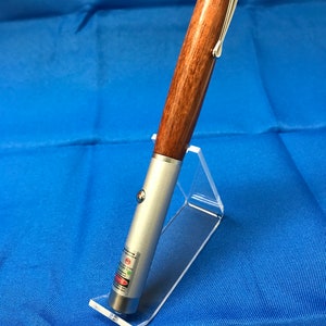 May include: A laser pointer with a wooden barrel and silver accents. The laser pointer is displayed on a clear acrylic stand against a blue background. The laser pointer has a silver clip and a red laser indicator.