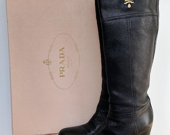 Botas altas de piel negra de Prada con tacón de bloque y logo dorado.