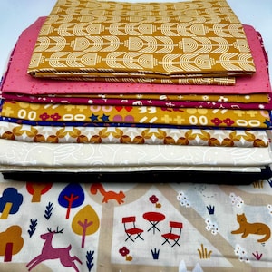 May include: A stack of various fabric pieces with different patterns. The top fabric is mustard yellow with a white geometric design. Other fabrics include pink, burgundy, and patterned designs with stars, flowers, and woodland creatures. The bottom fabric has a cream background with a forest scene.