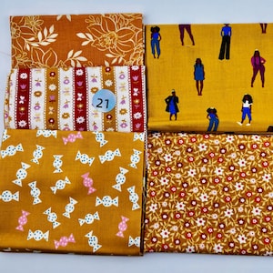 May include: Four folded fabric swatches featuring distinct patterns: a mustard yellow floral print, a red and white striped floral design with a circular number 21 tag, a mustard yellow background with scattered candy icons, and a dense floral pattern.