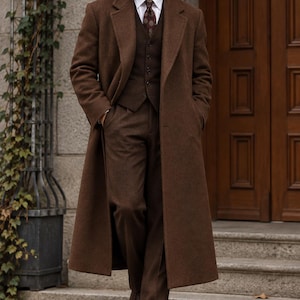 May include: A brown wool overcoat worn over a matching brown three-piece suit consisting of a vest and trousers, paired with a white collared shirt and a dark patterned necktie, complemented by dark brown leather dress shoes.
