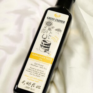 K&ouml;nnte beinhalten: Eine dunkle Glasflasche mit Green Farmer Sonnenblumenkern&ouml;l. Das Etikett zeigt Illustrationen von Sonnenblumen, einem Hufeisen und einem Fass. Die Flasche enth&auml;lt 250 ml kaltgepresstes, unraffiniertes &Ouml;l.